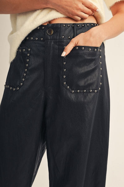 Close-up of a person wearing dark navy wide-leg pants with studded detailing around the waistband and front pockets, paired with a cream knit top against a plain light background.