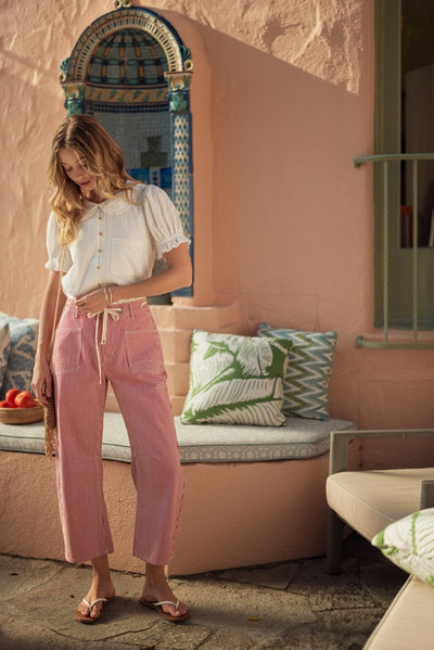 model wearing a red striped drawstring pants with a white blouse in front of architecture