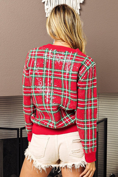 Person wearing a red plaid sweater with white accents in an indoor setting