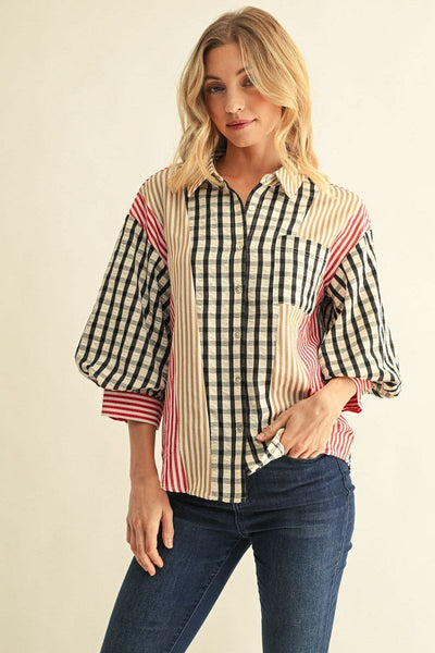 A woman modeling a long-sleeve button-up shirt with a mixed pattern design featuring a black and white gingham check, vertical beige and white stripes, and red pinstripes, paired with dark blue jeans against a light beige background.