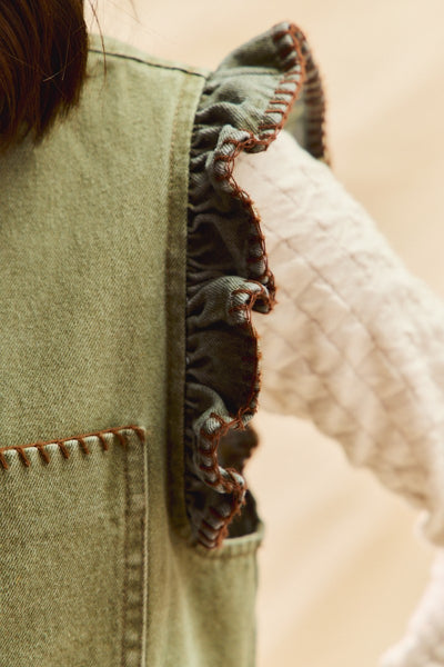 Close-up of a green denim jacket with ruffled trim on a blurred background