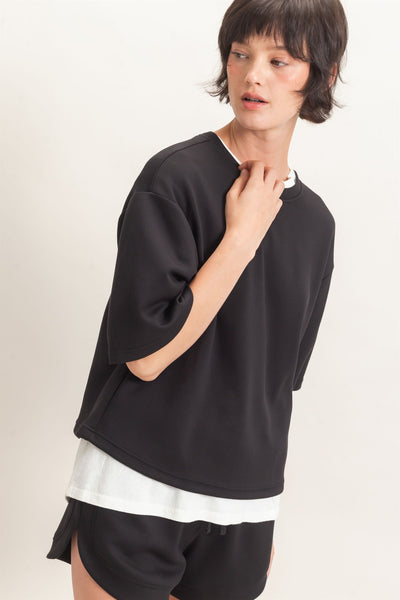 model wearing black short sleeve top with white tshirt underneath and black shorts in front of a light background