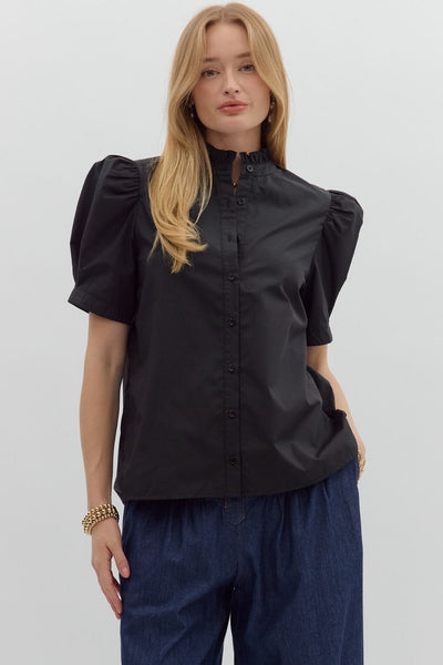 Woman wearing a black blouse with puffed sleeves and navy pants on a white background