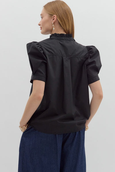 Woman wearing a black blouse with puffed sleeves and navy pants on a light gray background