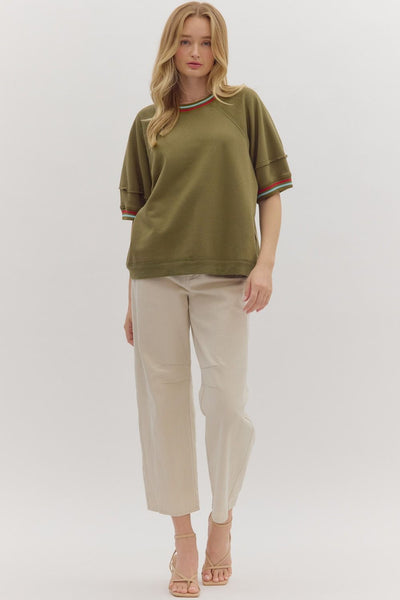 Woman wearing a green top with red and white trim and beige pants on a white background