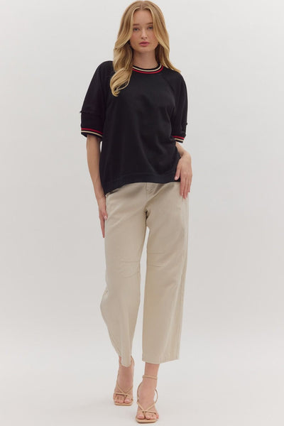 Woman wearing a black sweater with red and white trim and beige pants on a white background