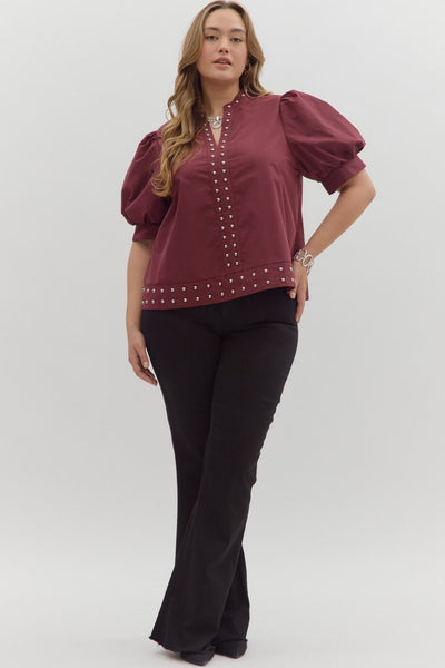 Woman wearing a burgundy blouse with pearl embellishments and black pants on a white background