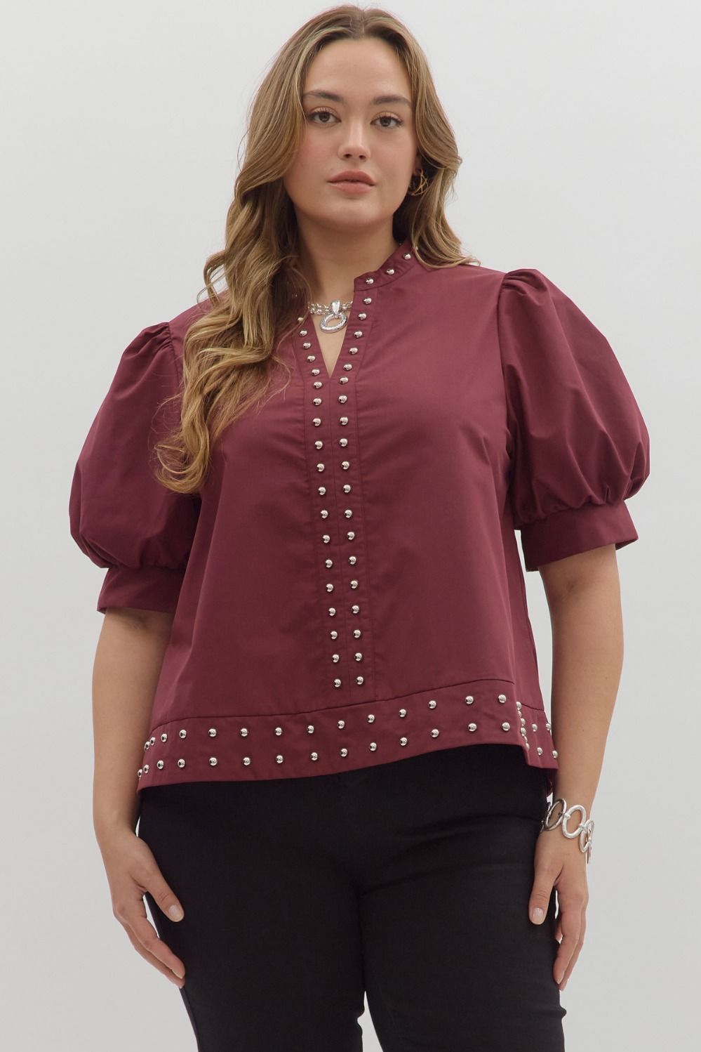 Woman wearing a burgundy blouse with puff sleeves and decorative buttons on a white background