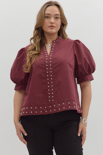 Woman wearing a burgundy blouse with puff sleeves and decorative buttons on a white background