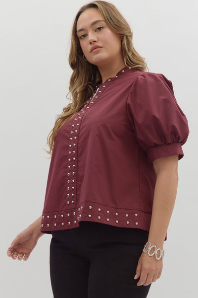Woman wearing a burgundy blouse with studded details on a white background