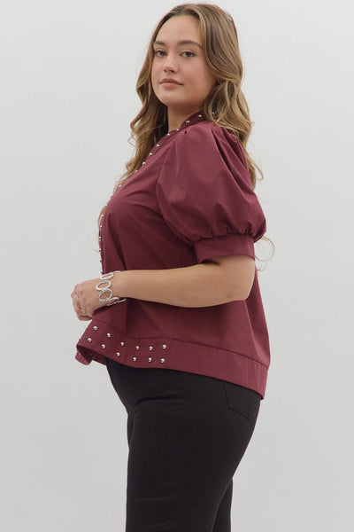 Woman wearing a burgundy blouse with pearl embellishments on a white background