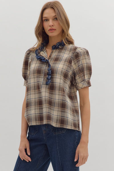 Woman wearing a plaid shirt with ruffled collar and blue jeans on a plain background