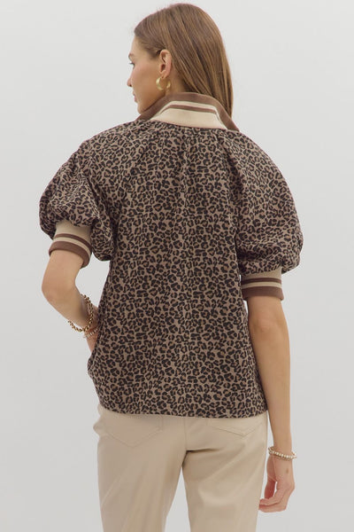 Person wearing a leopard print blouse with puff sleeves on a plain background