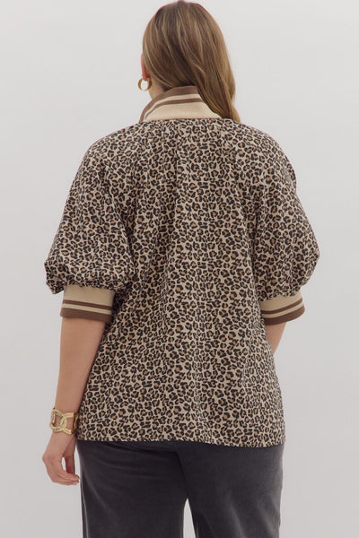 Person wearing a leopard print shirt with striped cuffs on a plain background