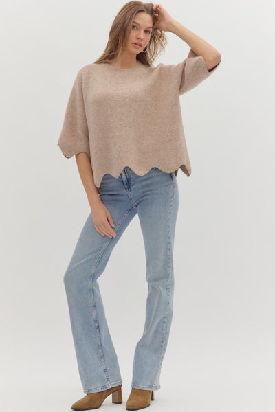 Woman wearing a beige sweater and light blue jeans on a white background