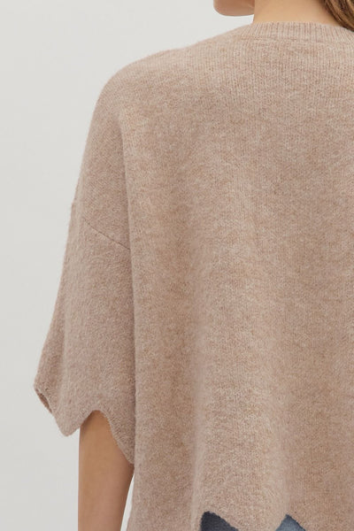 Beige poncho worn by a person on a plain background