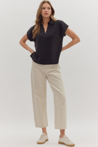 Woman wearing a black polo shirt and beige pants on a white background