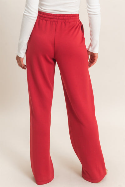 back of model wearing a white shirt & red pants with a light background