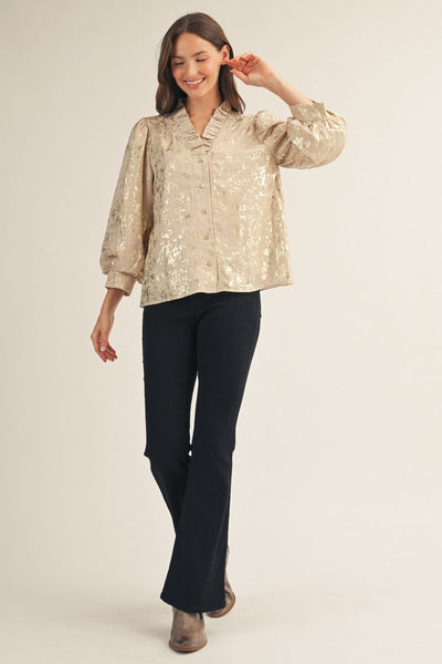 Woman wearing a beige metallic blouse with black pants on a plain background
