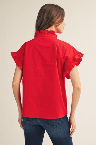 Woman wearing a red blouse with ruffled sleeves on a beige background