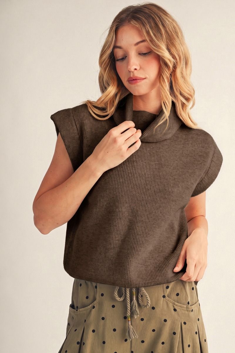 model wearing a cap sleeve turtleneck sweater with polka dot pants with beige background