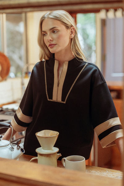 Woman in a black and beige top preparing coffee in a kitchen.