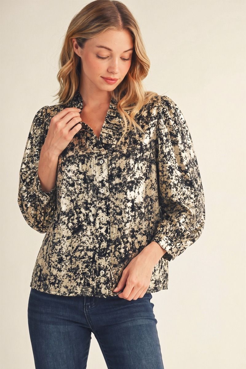 A woman wearing a long-sleeve button-up blouse with a black and beige abstract floral pattern, paired with dark blue jeans, against a plain beige background.