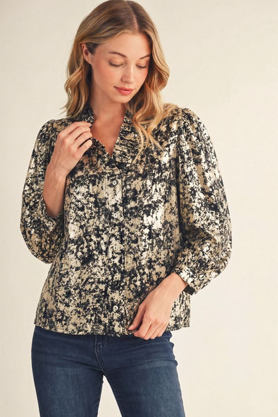 A woman wearing a long-sleeve button-up blouse with a black and beige abstract floral pattern, paired with dark blue jeans, against a plain beige background.