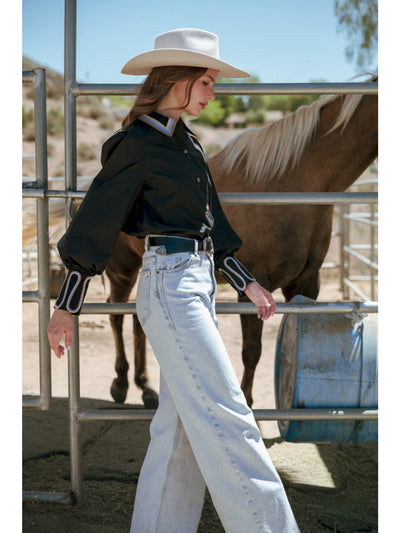 Woman in cowboy hat and black shirt standing next to a horse in an outdoor setting