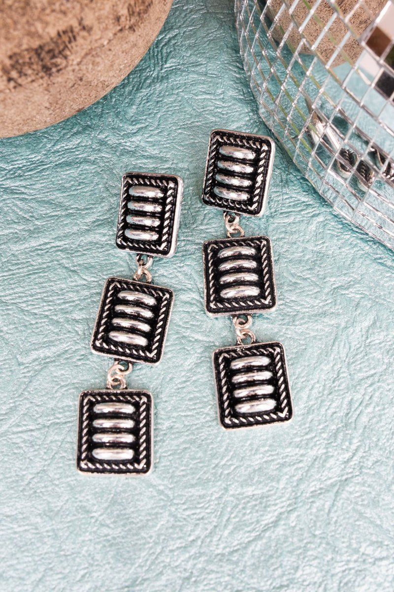 Silver square-shaped earrings on a textured surface