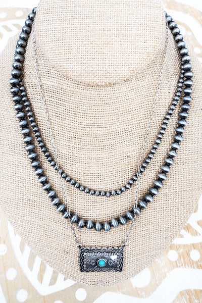 Triple strand necklace with scalloped bar pendant on bust display.
